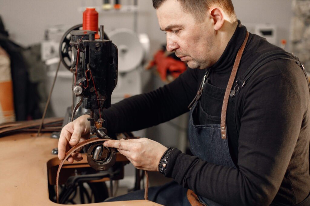 mature-craftsman-working-his-workspace-man-wearing-apron-using-sewing-machine-grounge-dark-stone-texture-background (1)